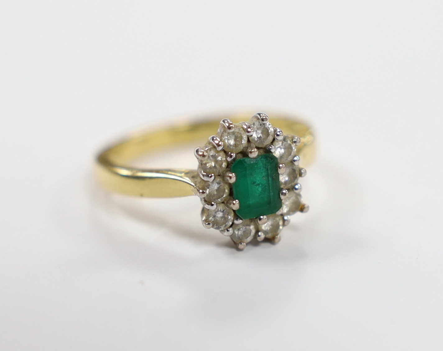 A modern 18ct gold, emerald and diamond set oval cluster ring, size L/M, gross weight 4.9 grams.